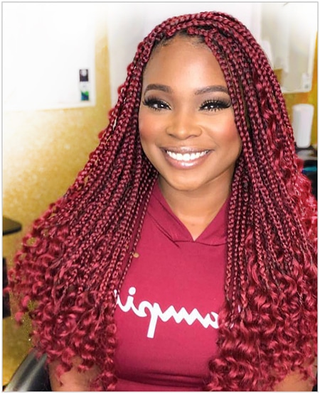 Smiling black women wearing goddess locs crochet box braids in red and burgundy colors while at a salon.